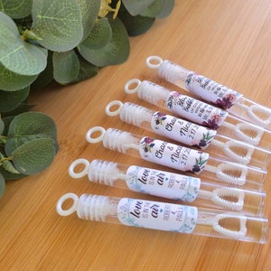 May include: Eight clear plastic bubble wands with white wands and floral patterned labels. The labels have the text "Love is in the air" and "Char & Nico 2.17.20" printed on them.