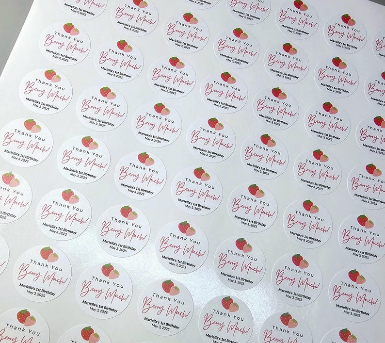 Może przedstawiać: Arkusz białych okrągłych naklejek z tekstem "Thank You" i "Berry Much!" w r&oacute;żowym piśmie. Naklejki przedstawiają grafikę truskawki w kolorze r&oacute;żowym i czerwonym oraz tekst "Mariella's 1st Birthday" i "May 3, 2023".