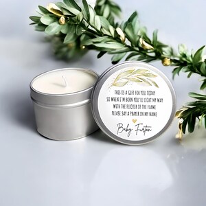 May include: A silver candle tin with a white candle and a lid with text and a gold leaf design. The text reads: "THIS IS A GIFT FOR YOU TODAY SO WHEN I'M BORN YOU'LL LIGHT MY WAY WITH THE FLICKER OF THE FLAME PLEASE SAY A PRAYER IN MY NAME Baby Furton."