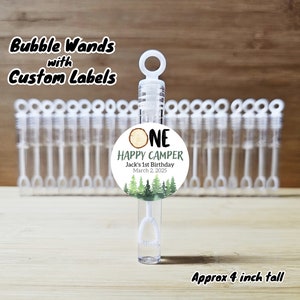May include: Clear bubble wands with custom labels. Each wand is approximately 4 inches tall. The label reads "ONE HAPPY CAMPER" with a forest graphic and the text "Jack's 1st Birthday March 2, 2025". The text "Bubble Wands with Custom Labels" is also visible.