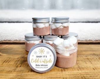 May include: A set of six clear glass jars with silver lids filled with hot chocolate mix and marshmallows. The jars have a white and gold snowflake themed label that reads "Baby It's Cold Outside" with the name "Baby Johnson" and the date "February 2024".
