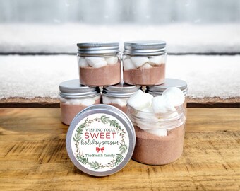 May include: Six clear glass jars with silver lids filled with hot chocolate mix and marshmallows. The jars have a white label with green and red holiday-themed graphics and the text "Wishing you a sweet holiday season. The Smith Family."