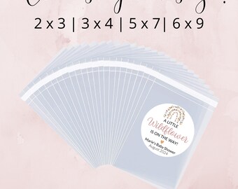 May include: A set of clear plastic favor bags with a round sticker attached to each bag. The sticker is white with a pink and gold floral design and the text "A Little Wildflower Is On The Way!" Marie's Baby Shower August 2024. The bags are available in various sizes: 2x3, 3x4, 5x7, and 6x9.