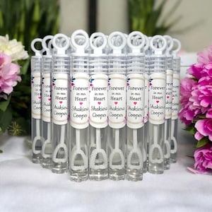 May include: A set of clear plastic bubble wands with white handles and personalized labels. The labels feature the text "Forever in our Heart" with the name "Shakiera Cooper" printed below.