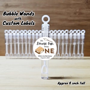 May include: A set of clear plastic bubble wands with a round, white label that says "It's S'more Fun being ONE" with a graphic of a s'more and the text "Milo's 1st Birthday August 6, 2025". The wands are approximately 4 inches tall.