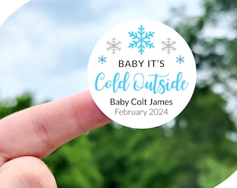 May include: A white circle sticker with blue snowflakes and the text "BABY IT'S Cold Outside" in black. The sticker also includes the text "Baby Colt James" and "February 2024". The sticker is available in sizes 1 inch, 1.5 inches, 1.75 inches, 2 inches, 2.25 inches, and 3.33 inches.