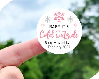 May include: A white circle sticker with pink and gray snowflakes and the text "BABY IT'S Cold Outside" in pink. The text "Baby Maybel Lynn February 2024" is also on the sticker. The sticker is 1 inch, 1.5 inches, 1.75 inches, 2 inches, 2.25 inches, or 3.33 inches in diameter.