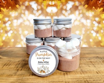 Op de afbeelding: Een kleine pompoen is onderweg!  Een set van zes kleine glazen potten met zilveren deksels gevuld met warme chocolademelk mix en marshmallows. De potten zijn versierd met een label waarop staat "Een kleine pompoen is onderweg! Baby Miller Februari 2024" met een pompoen- en herfstbladerenontwerp.