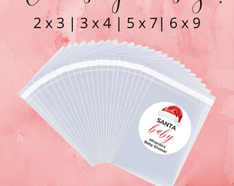 May include: A set of clear plastic favor bags with red and white Santa Baby labels. The labels feature a Santa hat and the text "Santa Baby" with a personalized name and the words "Baby Shower". The image shows various sizes available: 2x3, 3x4, 5x7, and 6x9.