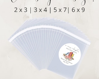 May include: A set of clear plastic bags with labels that say "a new chapter will soon begin" with a floral design and the text "Maria's Baby Shower May 2025". The bags are available in various sizes: 2x3, 3x4, 5x7, and 6x9 inches.