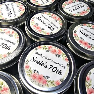 May include: A collection of small silver tins with floral designs and the text "Thank you for celebrating Susie's 70th" printed on the lids.