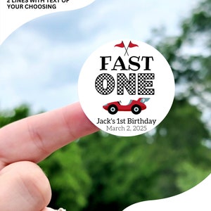 May include: Circle sticker with the text "FAST ONE" in black and white checkered font. A red race car with a number 9 is below the text. The text "Jack's 1st Birthday" and "March 2, 2025" are below the car. The sticker is available in sizes 1 inch, 1.5 inch, 1.75 inch, 2 inch, 2.25 inch, and 3.33 inch. The sticker pictured is 2 inches.
