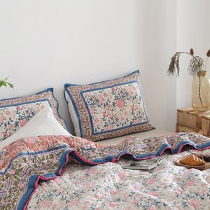 May include: A bed with a floral patterned quilt and two matching pillowcases. The quilt features pink and green floral designs on a white background, with blue and pink borders. A white pillow is placed between the pillowcases.