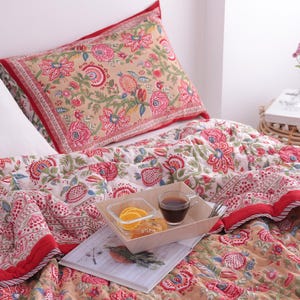 Peut inclure: Un lit avec une courtepointe et des taies d'oreiller à motifs floraux dans les tons de rouge, rose, vert et beige. Un plateau avec de la nourriture et des boissons est posé sur la courtepointe. Un oreiller blanc est visible.
