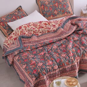 May include: A floral quilt and pillow set in grey, cream, and red. The bedding features a detailed floral pattern and a contrasting border. The set includes a quilt and two matching pillowcases, creating a cohesive bedroom aesthetic.
