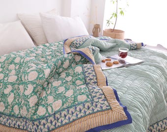 May include: A bed is covered with a green floral patterned quilt and white pillows. The quilt has a blue border with a tan and white striped pattern. A glass of tea and cookies sit on a magazine.