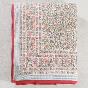 Puede incluir: Un edredón con estampado floral con fondo blanco y detalles en rosa, verde y azul. El edredón tiene un borde rojo y un patrón de rayas en los bordes. El diseño floral se repite en todo el edredón.