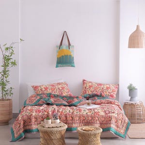 May include: A bedroom scene featuring a floral patterned quilt and matching pillows in shades of red, pink, and teal. Two small woven stools sit at the foot of the bed. A tote bag with a Nashville skyline hangs on the wall.