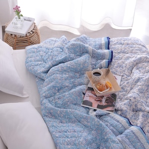 May include: A light blue and white floral patterned quilt covers a bed, with white pillows and a small side table. A tray with coffee, pastries, and a magazine rests on the quilt. The quilt has a blue border.