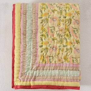 May include: A yellow floral quilt with pink and green accents. The quilt features a repeating pattern of flowers and leaves on a yellow background. The edges are trimmed with a red border and a yellow border. The quilt is likely made of cotton or a similar fabric.