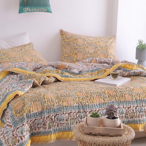 May include: A bed with a yellow, blue, and brown floral patterned quilt and matching pillowcases. The quilt has a yellow border and a detailed design. A small pillow with the word "Nashville" is visible.