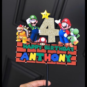 May include: A cake topper featuring Mario, Luigi, Yoshi, and Bowser characters from the Super Mario Bros. video game. The topper also includes a gold glitter number 4 and a brick wall with the words "Happy Birthday Anthony".