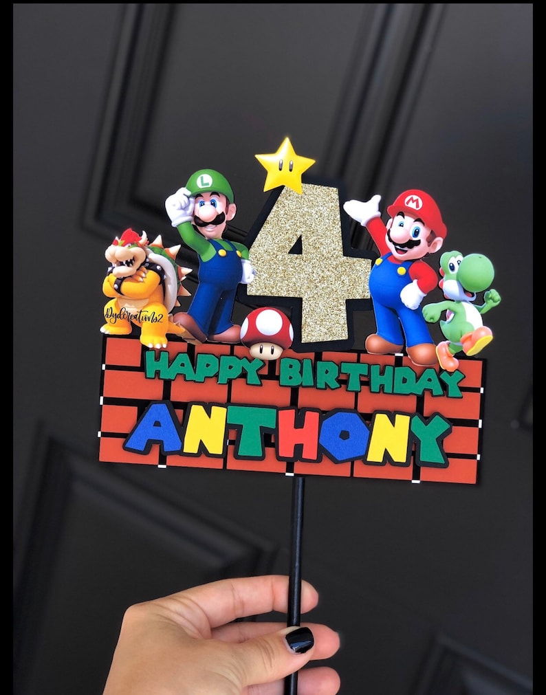 May include: A cake topper featuring Mario, Luigi, Yoshi, and Bowser characters from the Super Mario Bros. video game. The topper also includes a gold glitter number 4 and a brick wall with the words "Happy Birthday Anthony".