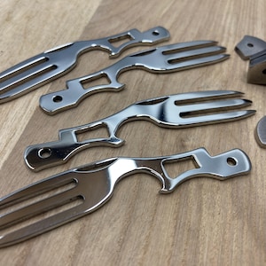 May include: Five silver metal utensils with a fork and a bottle opener design. The utensils are arranged on a wooden surface.