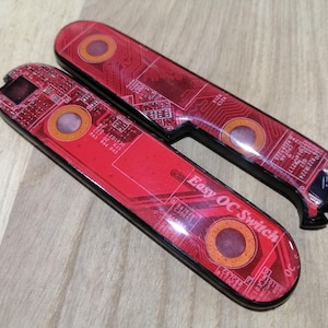 May include: Two elongated, rectangular switch covers featuring a red printed circuit board pattern. The surface displays orange circular accents and the white text "Easy OC Switch" printed on the lower piece. Both items have a glossy finish.
