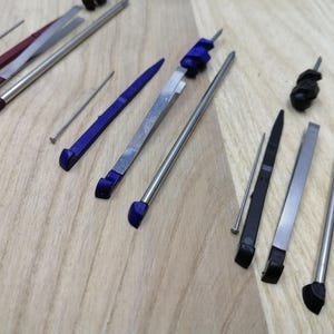 May include: A set of tools for watch repair, including a screwdriver, tweezers, and a small pin. The tools are made of metal and have a variety of tips.