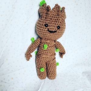 May include: A brown crocheted plush toy of a character with green leaves. The character has a smiling face with black eyes and a black mouth.