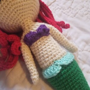 May include: Crocheted mermaid doll with red hair, a purple top, and a green tail with a light blue trim.