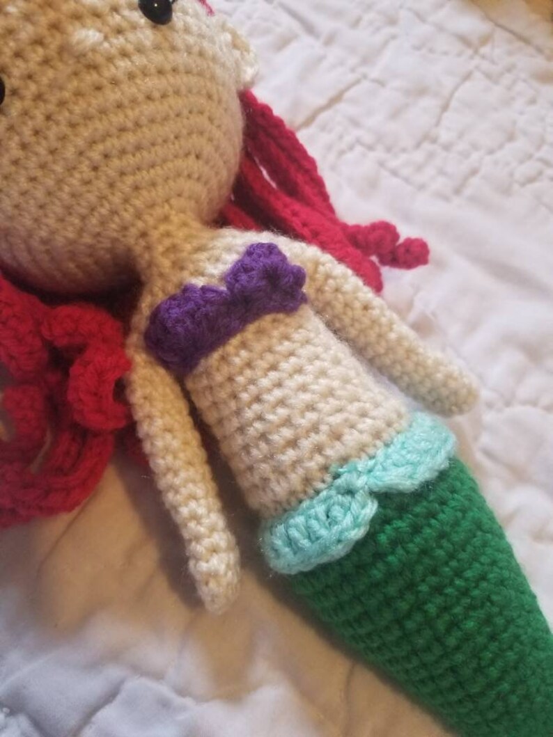 May include: Crocheted mermaid doll with red hair, a purple top, and a green tail with a light blue trim.