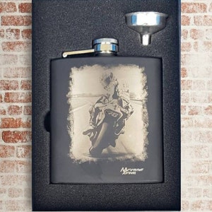 May include: A black stainless steel flask with a motorcycle rider image engraved on the front. The flask comes with a silver funnel and is packaged in a black box.