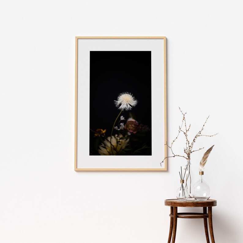 May include: A framed photograph of a white flower with a dark background. The flower is in focus and the background is blurred. The frame is light wood.