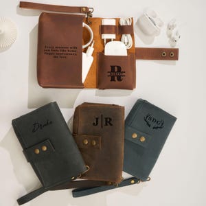 May include: A collection of leather tech organizers in various colors, including brown, black, and teal. The open brown organizer displays charging cables, a charger, and a wireless charging pad. The text "Every moment with you feels like home. Happy anniversary, my love." is visible.