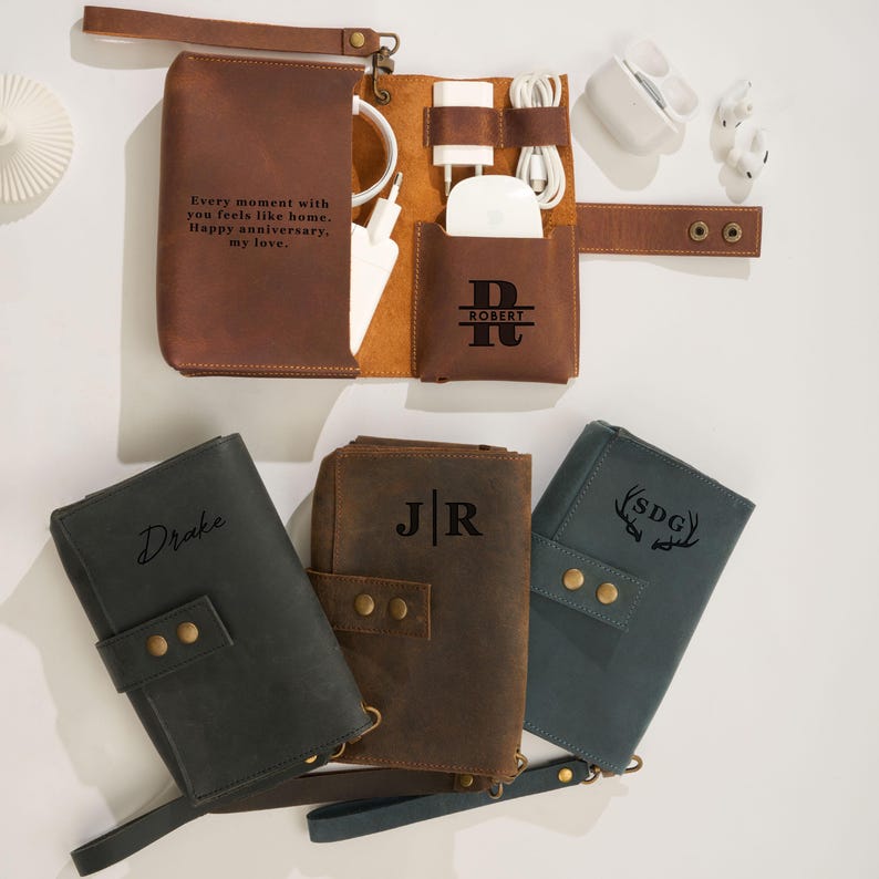 May include: A collection of leather tech organizers in various colors, including brown, black, and teal. The open brown organizer displays charging cables, a charger, and a wireless charging pad. The text "Every moment with you feels like home. Happy anniversary, my love." is visible.