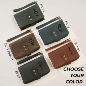 May include: A collection of leather wristlet wallets in various colors: forest green, navy, dark brown, black, and brown. Each wallet features a wrist strap, snap closure, and personalized initials or names. The text "CHOOSE YOUR COLOR" is also visible.