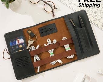May include: A black and brown leather tech organizer with a personalized nameplate. It holds cards, keys, and various tech accessories like earbuds and charging cables. The text on the organizer says, "This is just the beginning...I know you'll do great things ahead. Congratulations on your new job!"