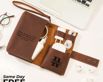 May include: A brown leather tech organizer with a wrist strap, holding chargers and accessories. The organizer has the text "Every moment with you feels like home. Happy anniversary, my love." and a monogram with the name "ROBERT".