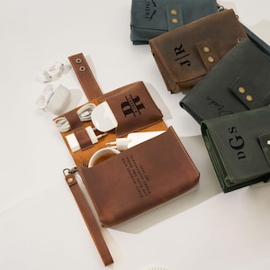 May include: A collection of personalized leather tech organizers in various colors, including brown and green. The organizers are open, displaying charging cables and a charger. Some have initials or names engraved, and one has a quote.