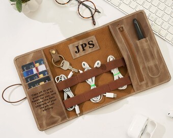 May include: A brown leather roll-up organizer with multiple compartments. It features a zippered pocket, card slots, and straps to hold cables and accessories. The organizer is personalized with the initials "JPS" and includes the text "Caps off to you, graduate! I'm so happy for you..."