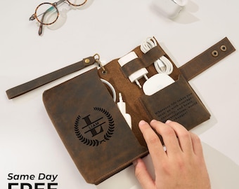 May include: A brown leather tech organizer with the name "LIAM" and a laurel wreath design. The organizer holds a charger, cables, and a white charging pad. The text "Wherever life takes you next..." is visible.