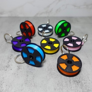 Puede incluir: Ocho carretes de hilo de colores con bobinas de plástico negro y llaveros plateados. Los carretes son naranja, amarillo, rosa, verde, blanco, azul, morado y rojo.