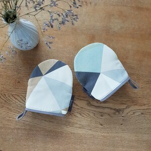 May include: Two oven mitts with a geometric pattern in shades of blue, gray, and beige. The mitts have a gray trim and a hanging loop.