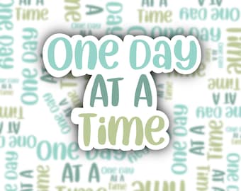 May include: A white sticker with the phrase "One Day AT A Time" in teal and green lettering. The background features a repeating pattern of the same text in a faded, blurred style.