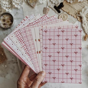 Può includere: Una collezione di cartoncini rettangolari con vari motivi rosa e bianchi, tra cui griglie con piccoli fiocchi, strisce verticali con minuscole fragole, disegni a quadretti e sfondi bianchi con piccoli cuori rossi.