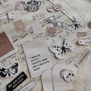 May include: A collection of vintage-style paper ephemera with a whimsical theme. The ephemera includes a teapot, butterflies, stamps, and a quote about waking up with a peaceful mind. The ephemera is on a sheet of music with a brown background.