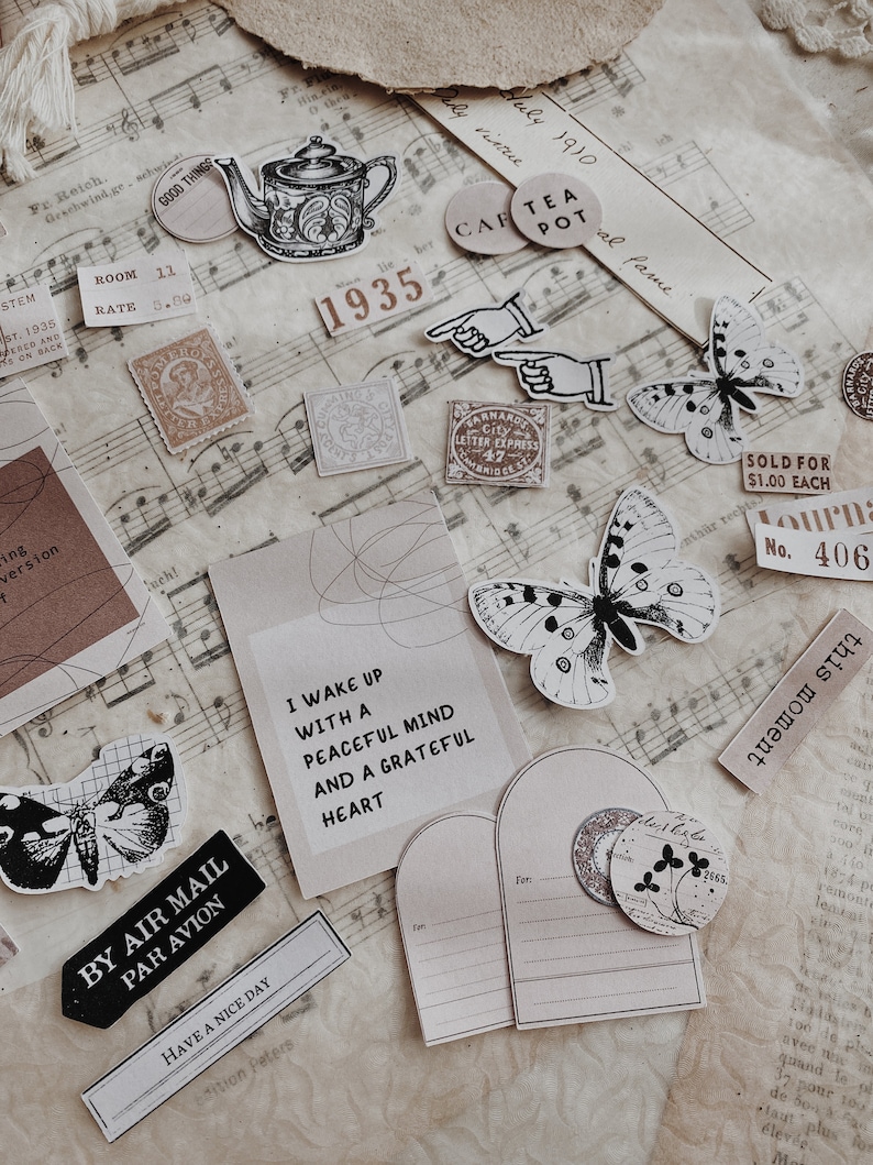 May include: A collection of vintage-style paper ephemera with a whimsical theme. The ephemera includes a teapot, butterflies, stamps, and a quote about waking up with a peaceful mind. The ephemera is on a sheet of music with a brown background.