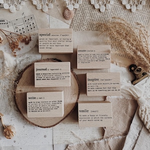 Puede incluir: Bloques de madera con definiciones de palabras como "especial", "crear" y "diario" dispuestos sobre un fondo de tonos neutros. Los bloques tienen texto negro y están rodeados de elementos decorativos.